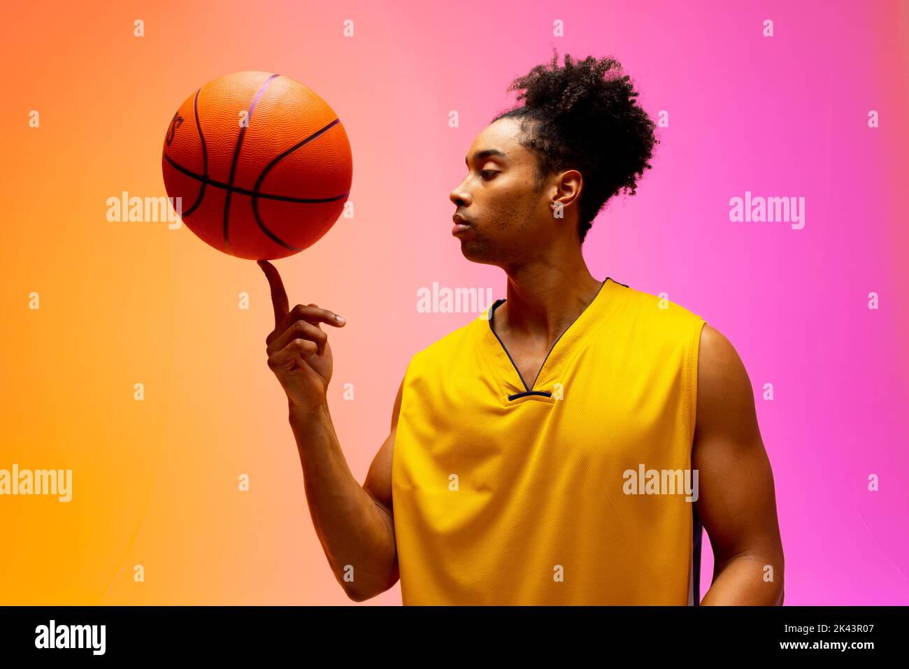 Image of biracial basketball player spinning basketball on pink to orange background. Sports and competition concept. Stock Photo