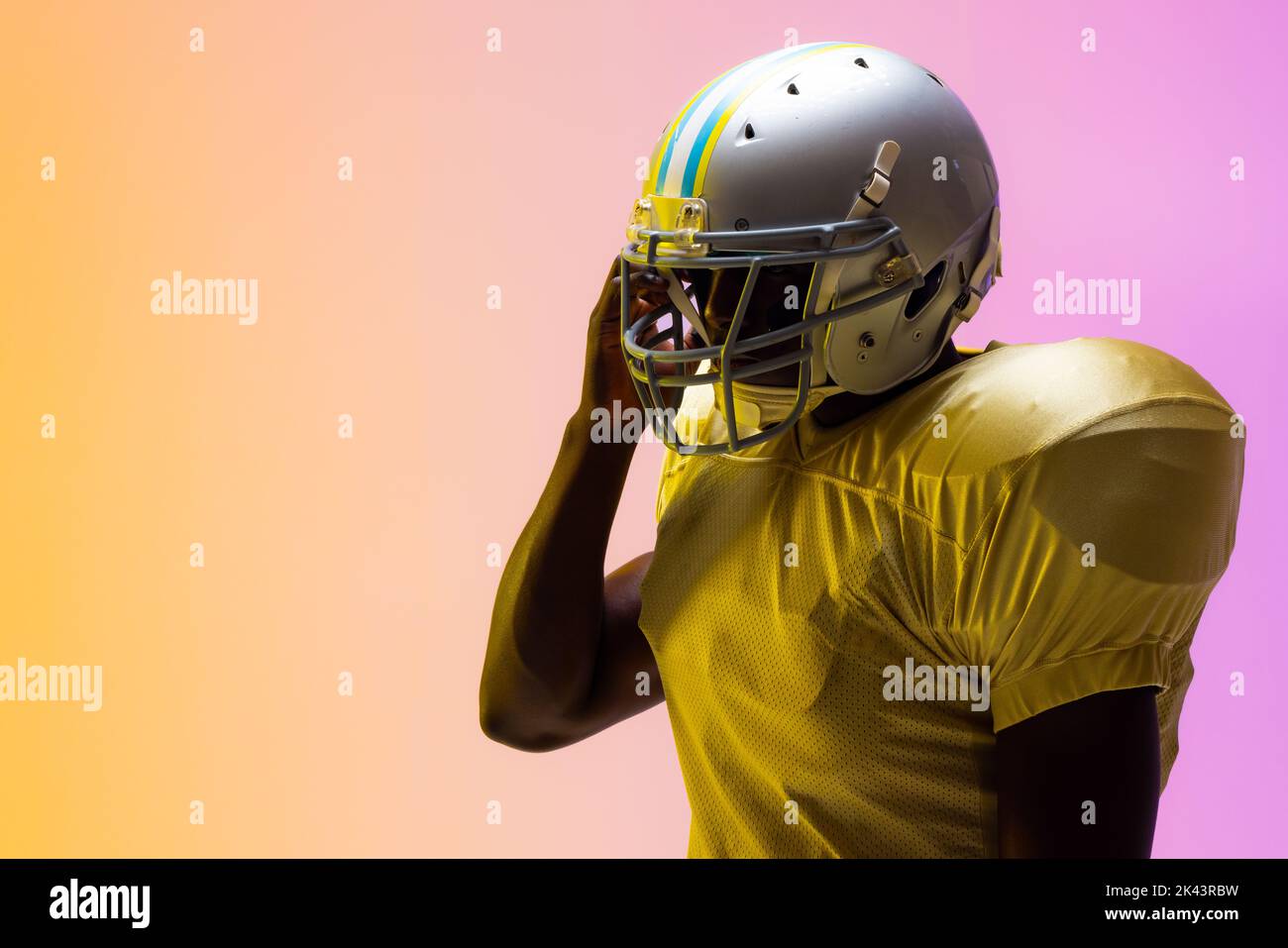 African american male american football player wearing helmet with neon yellow and purple lighting. Sport, movement, training and active lifestyle con Stock Photo