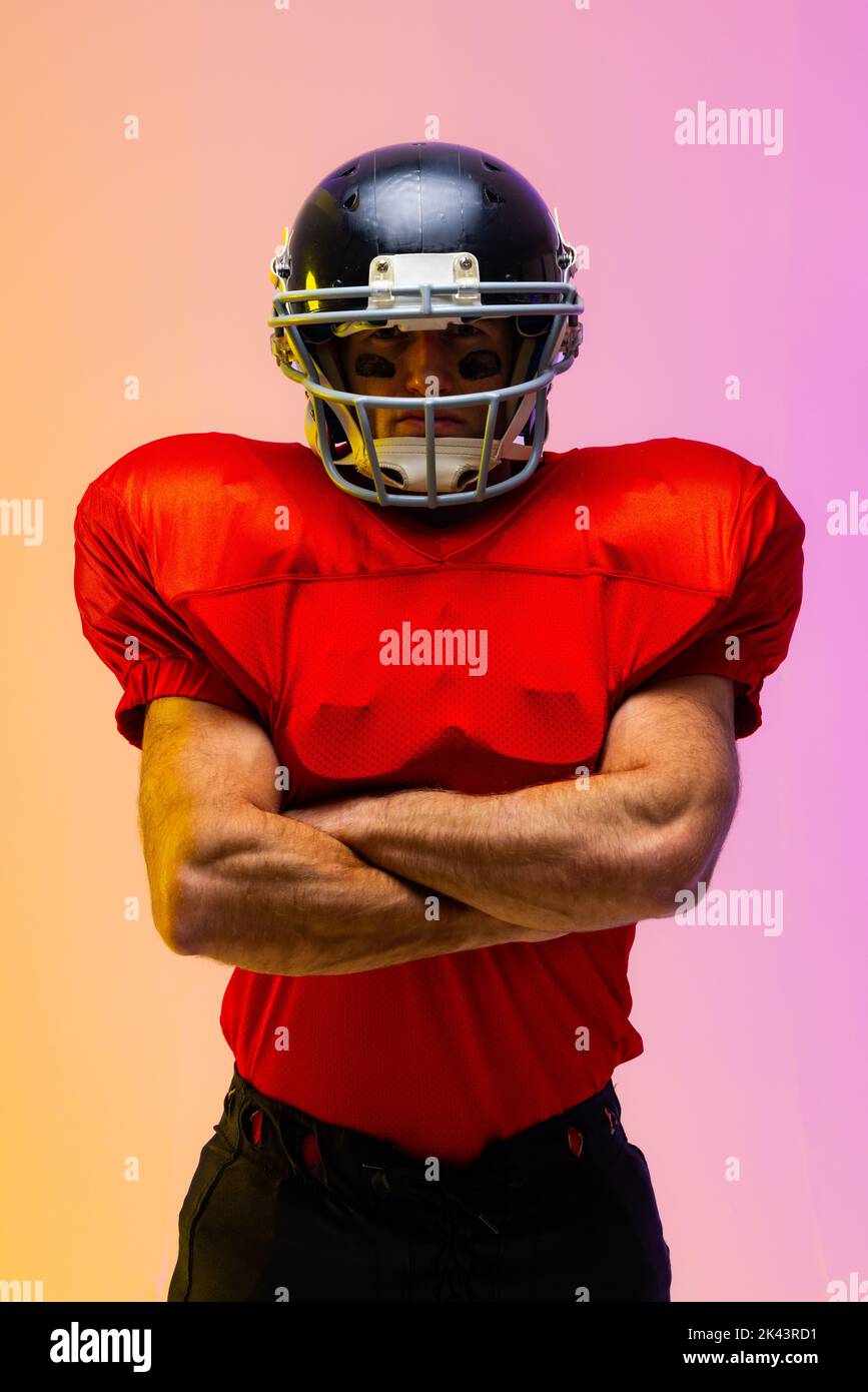 Caucasian male american football player wearing helmet with neon yellow and purple lighting. Sport, movement, training and active lifestyle concept. Stock Photo