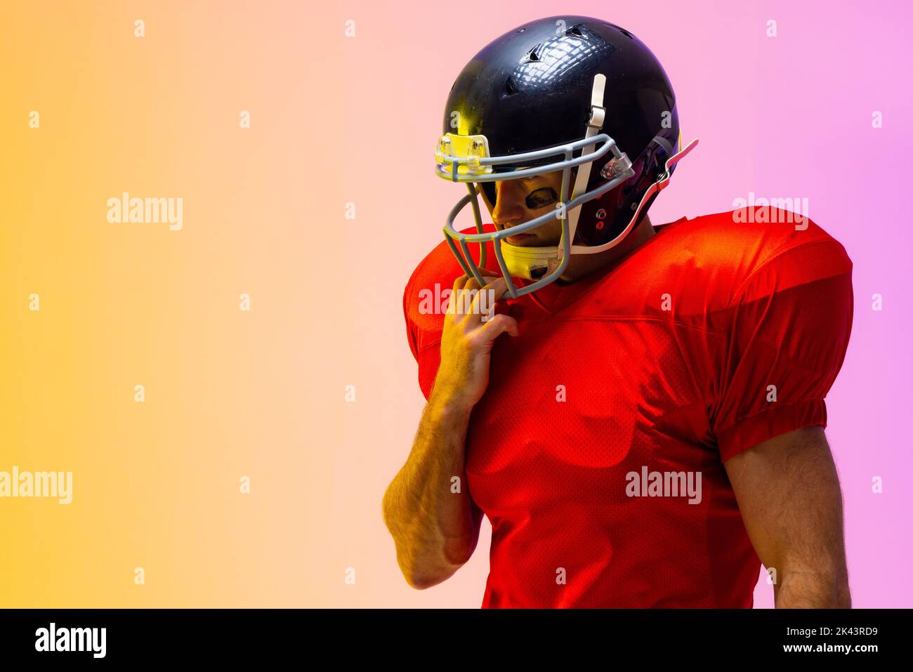 Caucasian male american football player wearing helmet with neon yellow and purple lighting. Sport, movement, training and active lifestyle concept. Stock Photo