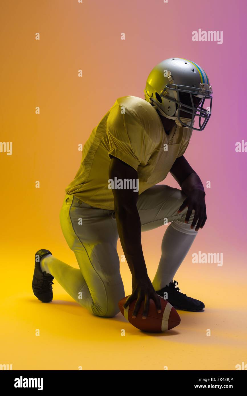 African american male american football player holding ball with neon yellow and purple lighting. Sport, movement, training and active lifestyle conce Stock Photo