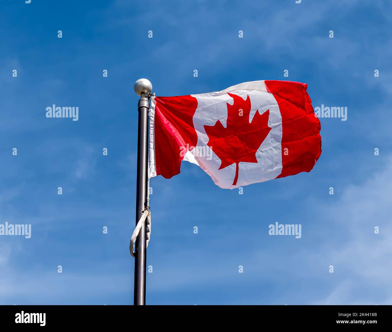 The Canadian flag flying on the top of a flagpole with a bright blue