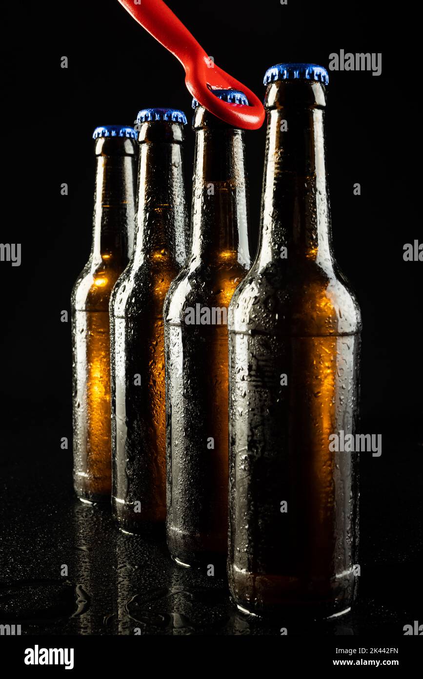 Image of red bottle opener and four beer bottles with blue crown caps, with copy space on black Stock Photo