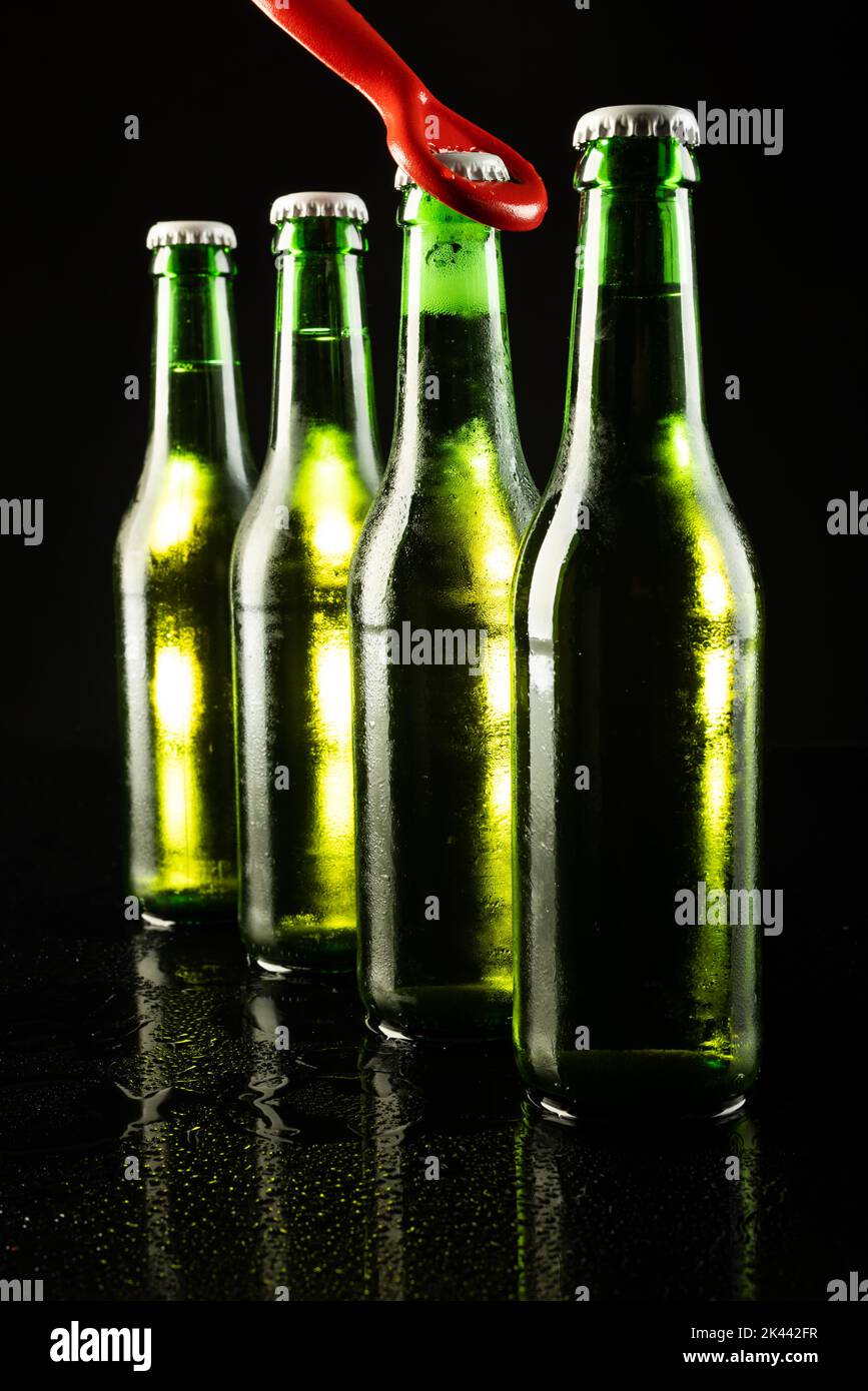Image of red bottle opener and four green beer bottles with crown caps, with copy space on black Stock Photo
