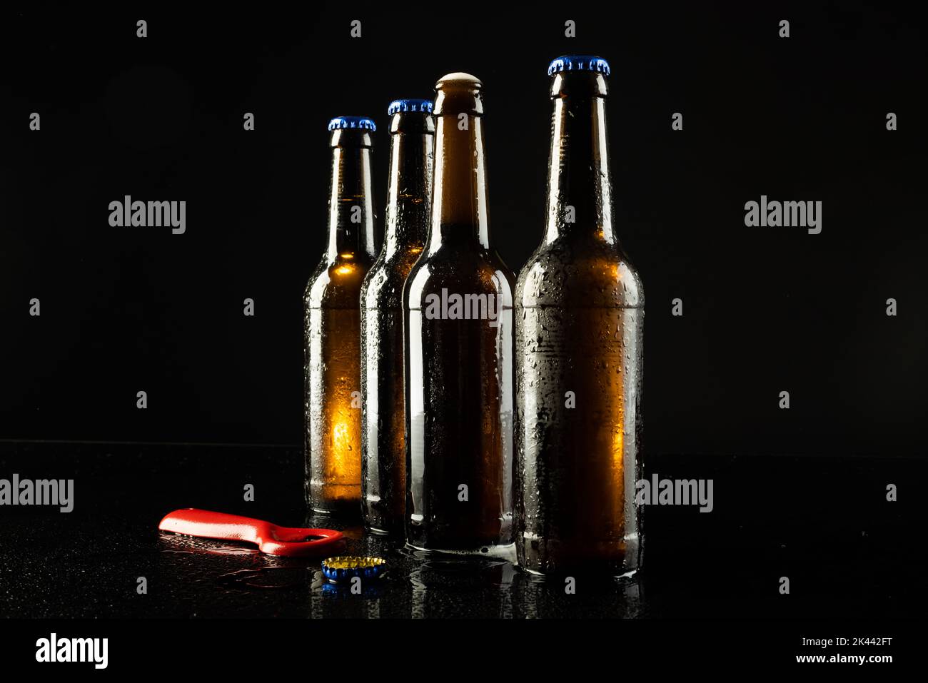 Image of red bottle opener and four beer bottles one open, with copy space on black Stock Photo