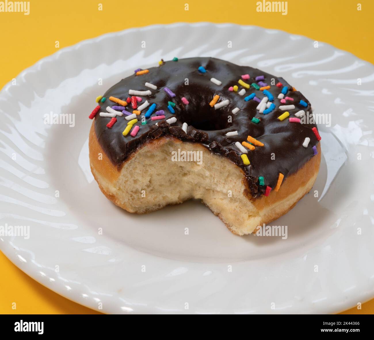 Eaten donut with chocolate icing and sprinkles on white plate Stock Photo