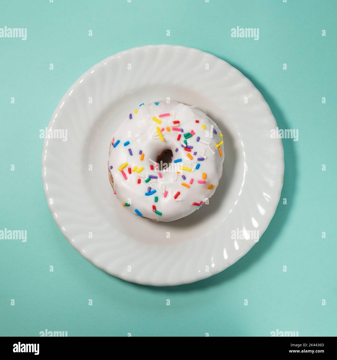 Overhead view of donut with white icing and sprinkles on white plate Stock Photo