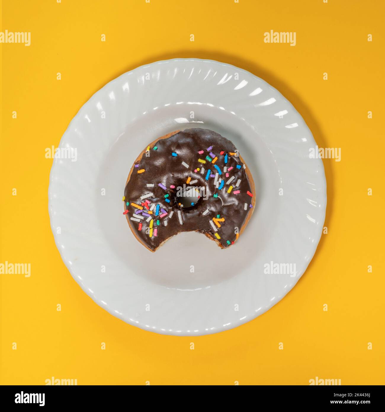 Overhead view of eaten donut with chocolate icing and sprinkles on white plate Stock Photo
