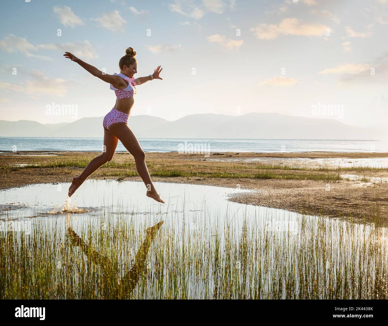 Teenage girl (14-15) in bikini jumping above lake at sunrise Stock Photo
