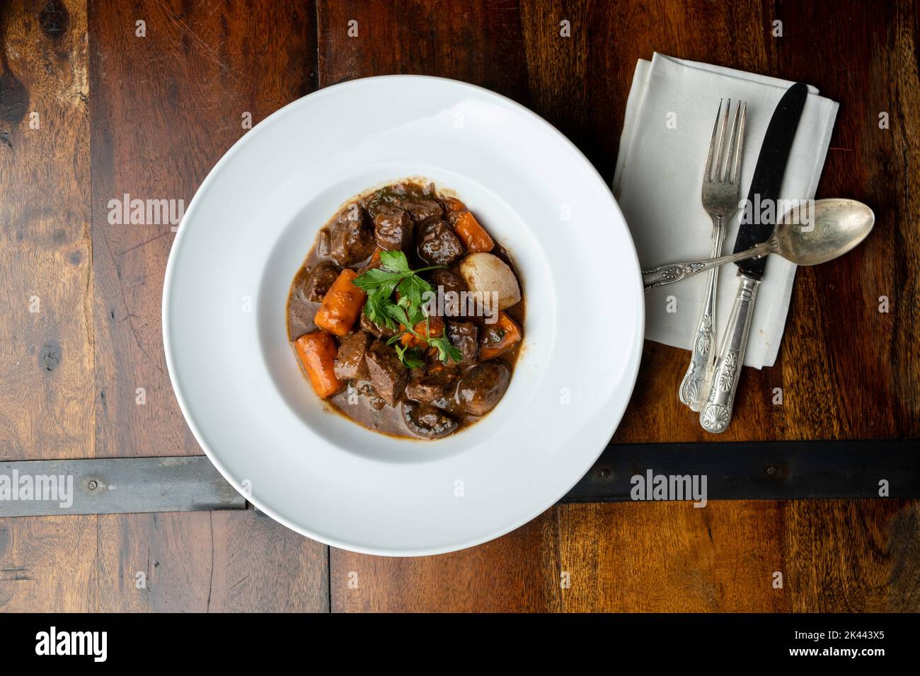 A white bowl of Boeuf Buorguignon - French Beef Stew - On a rustic wooden table, with a napkin and silverware Stock Photo