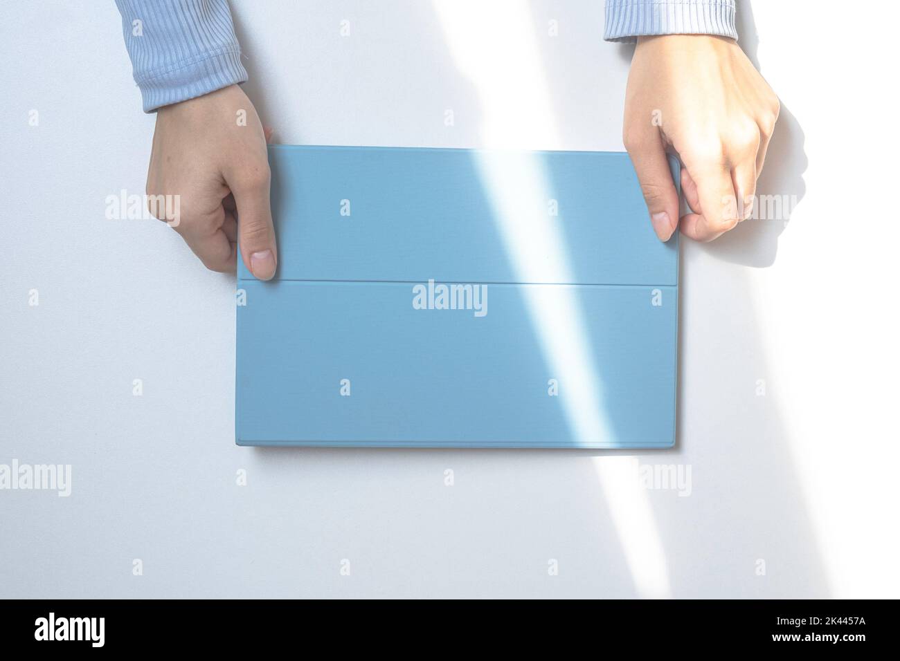 A tablet in a blue case on a white desk. The lights of a sun. The girl's hands are holding a tablet. top view Stock Photo