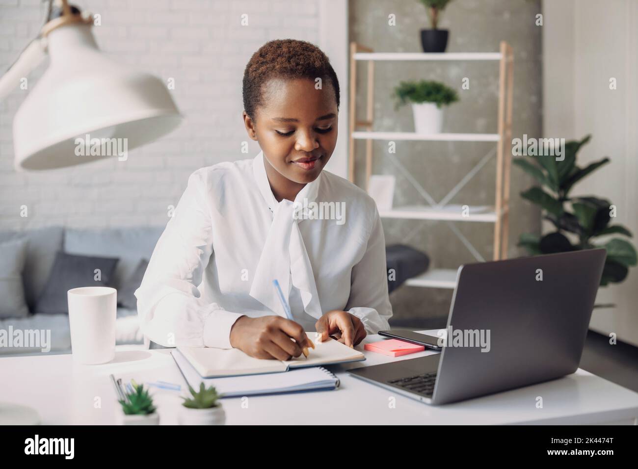 Confident and smiling portrait of an african businesswoman, working writing ideas in notebook at an office. Analyzing marketing charts, using sticky Stock Photo