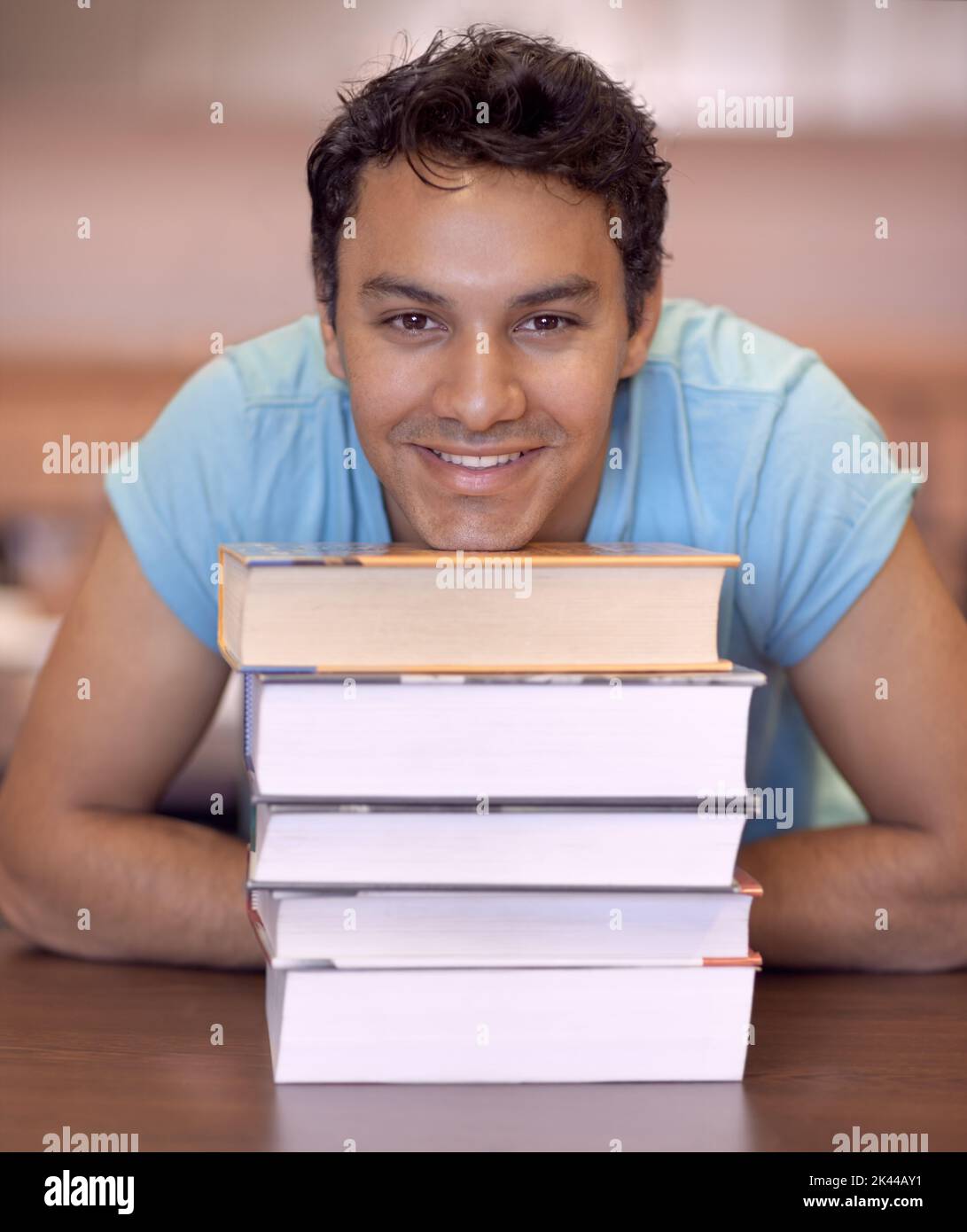 Hes eager to learn. Portrait of a young man sitting down and resting his head on some textbooks. Stock Photo