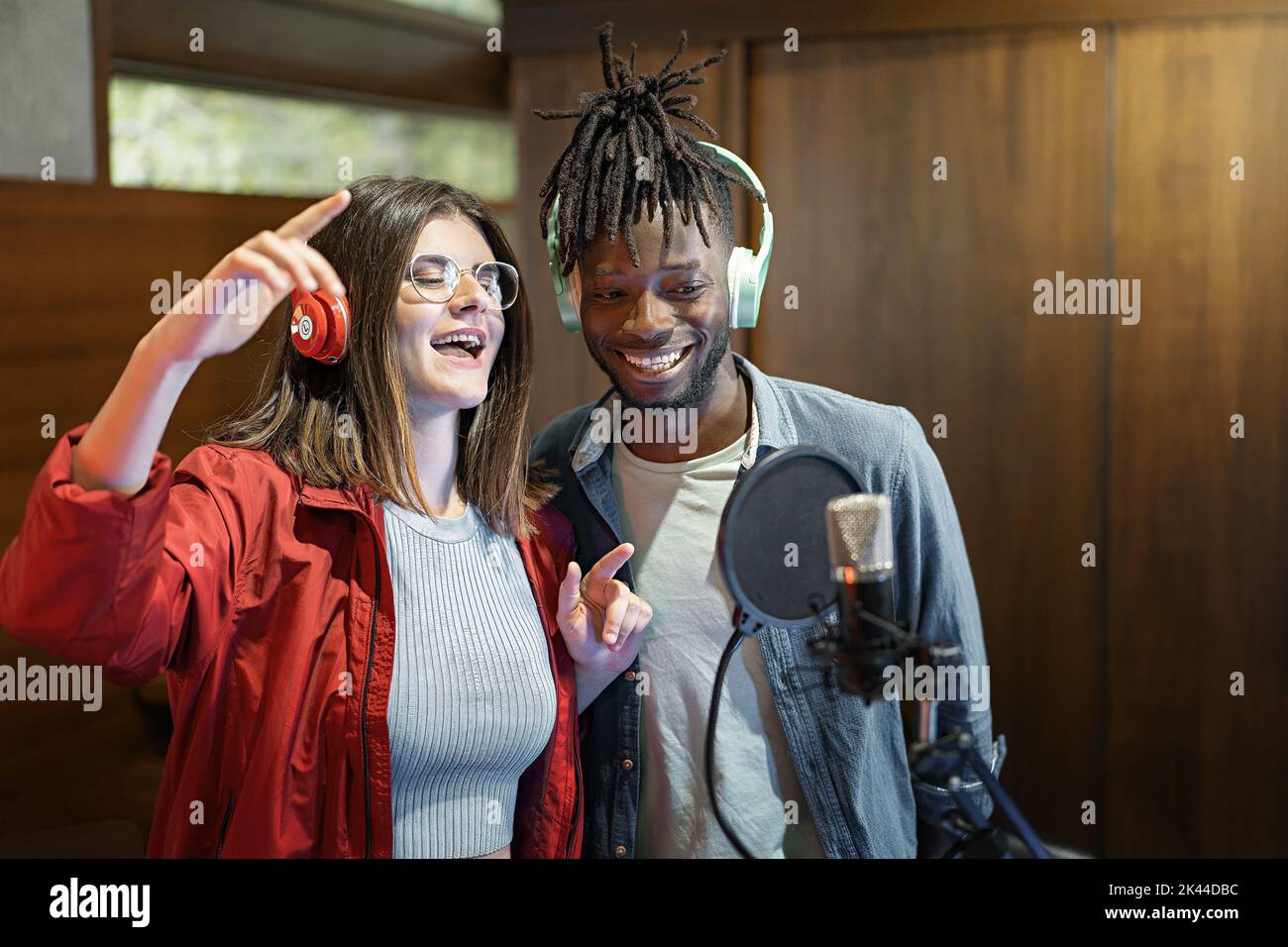 Excited multiethnic couple with microphone and headphones of young broadcasters singing music live and having fun - Social network content creators du Stock Photo