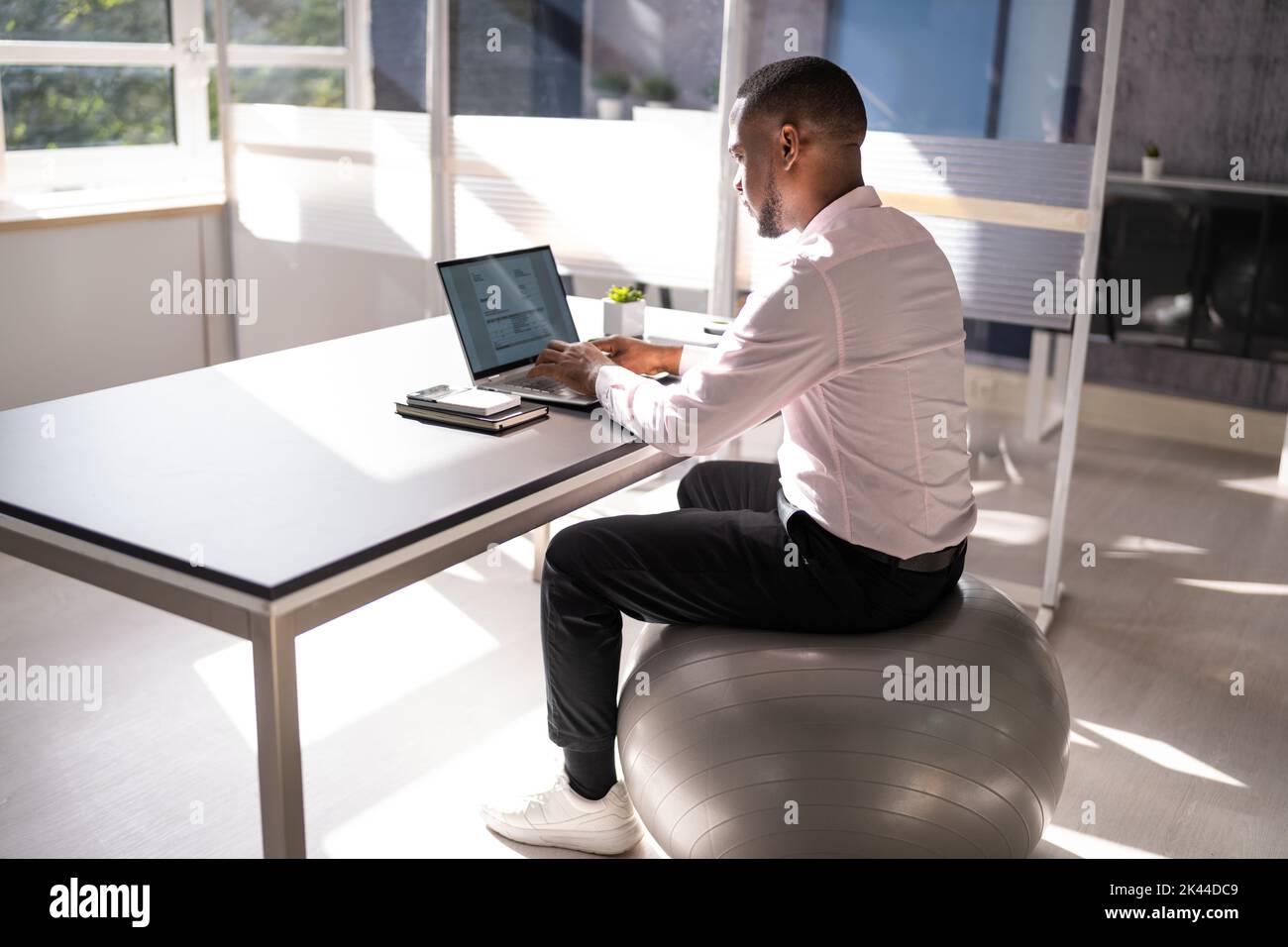 Correct Posture At Desk In Office Using Fitness Ball Stock Photo