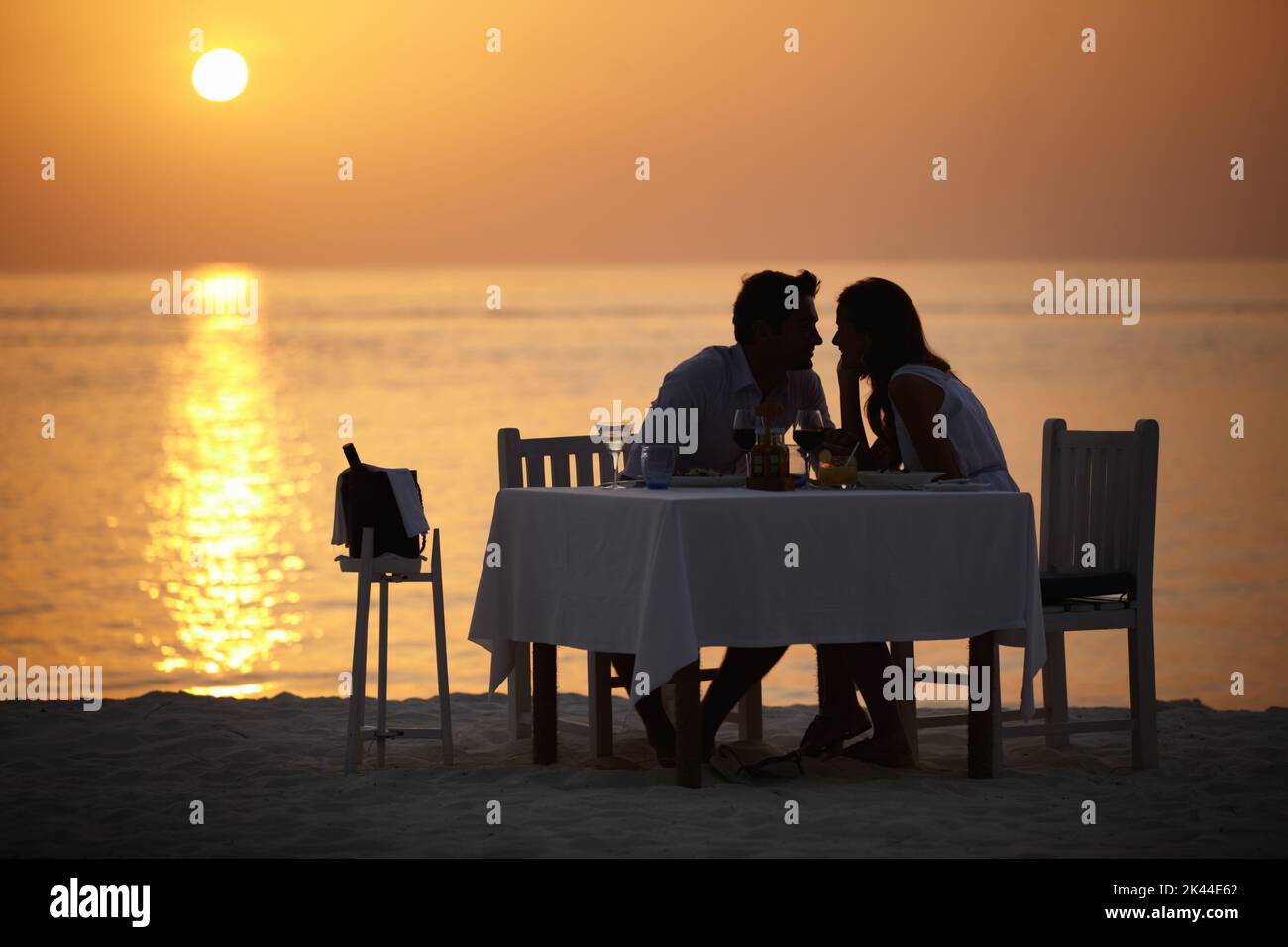 Maldivian silhouette. A young couple gazing into each others eyes while having dinner on the beach. Stock Photo