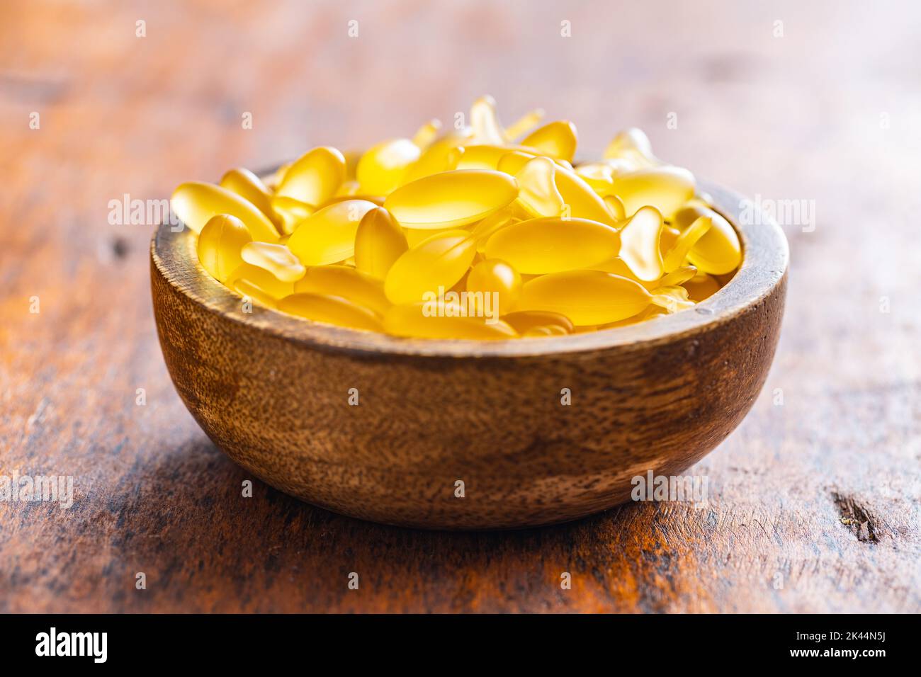 Fish oil capsules in bowl. Yellow omega 3 pills on the wooden table. Stock Photo