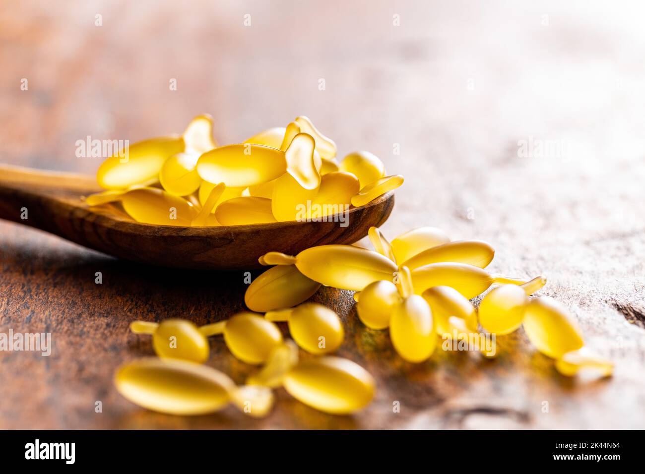 Fish oil capsules in spoon. Yellow omega 3 pills on the wooden table. Stock Photo