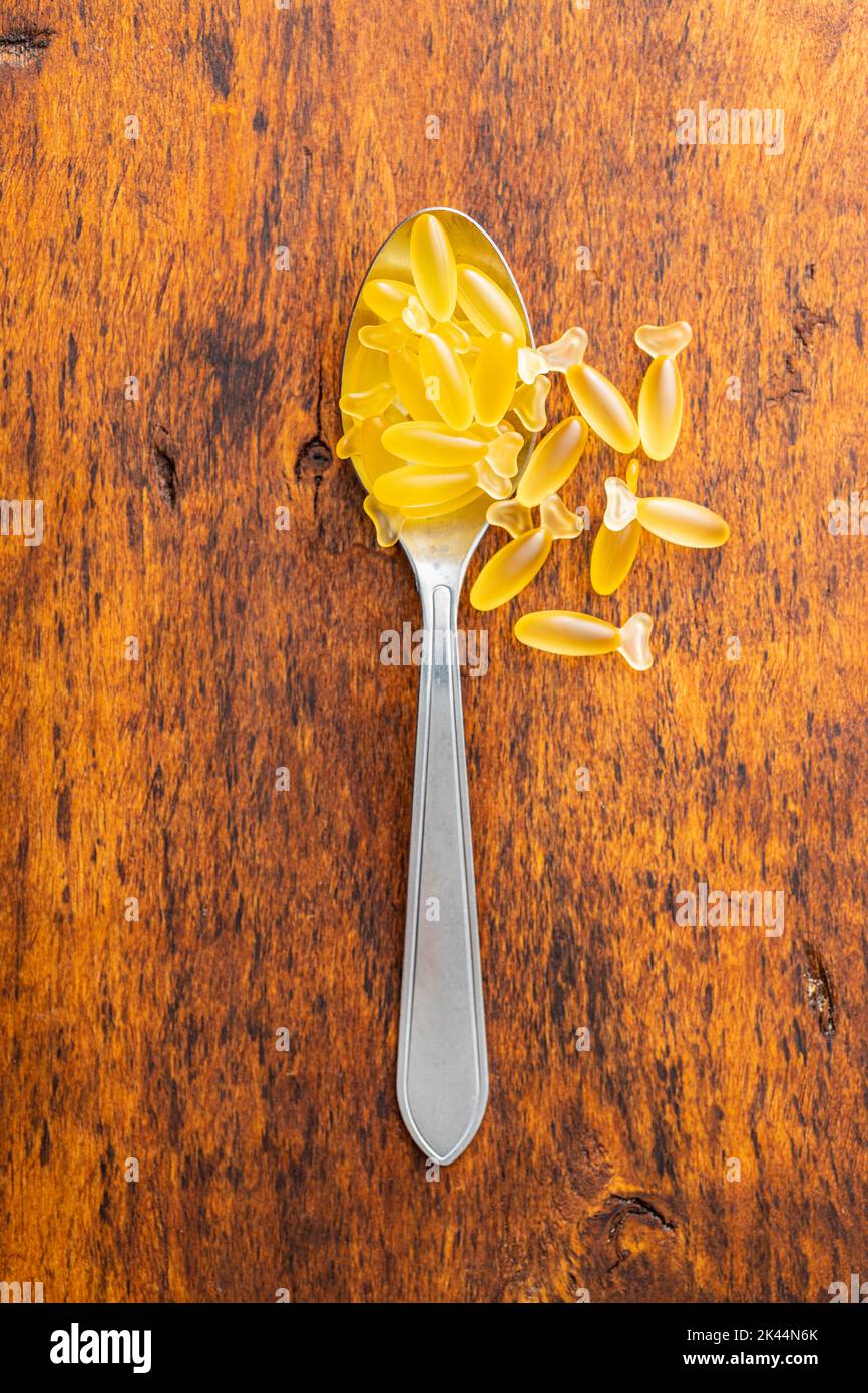 Fish oil capsules in spoon. Yellow omega 3 pills on the wooden table. Top view. Stock Photo