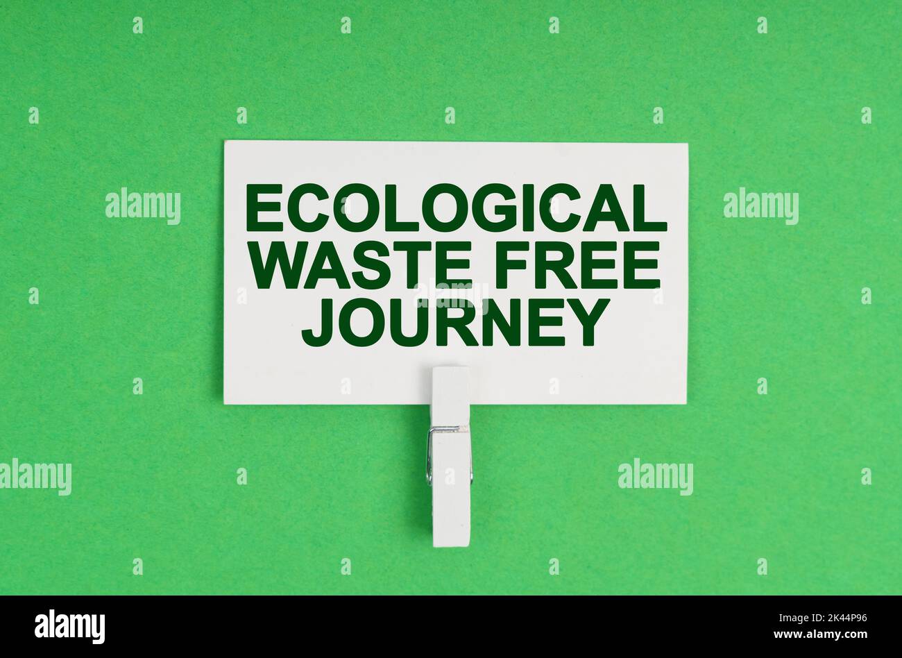 Ecology concept. On a green background, a business card on a clothespin. The business card says - Ecological Waste Free Journey Stock Photo