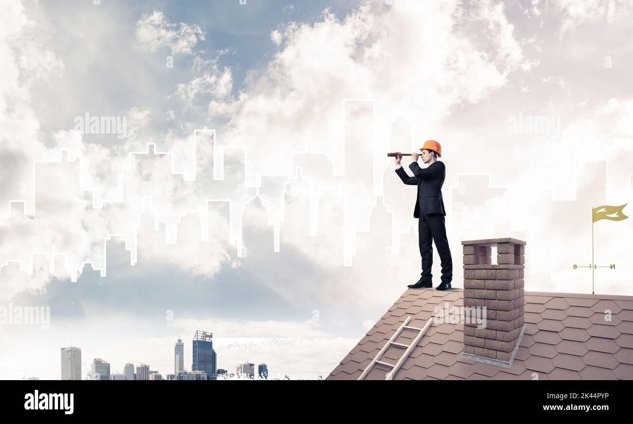 Engineer man standing on roof and looking in spyglass. Mixed med Stock Photo