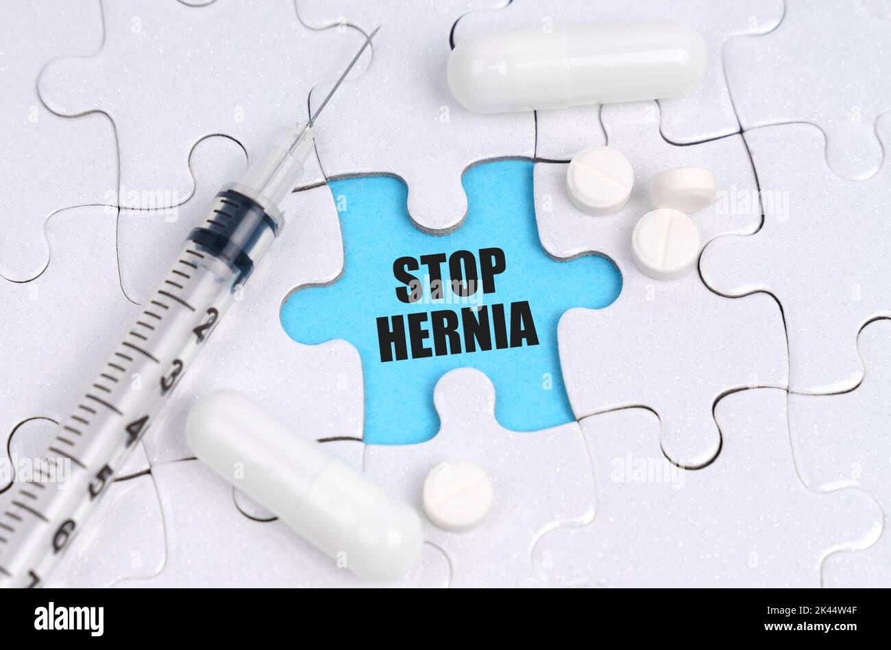 Medicine concept. There are pills and a syringe on the white puzzles. Inside on a blue background the inscription - STOP HERNIA Stock Photo
