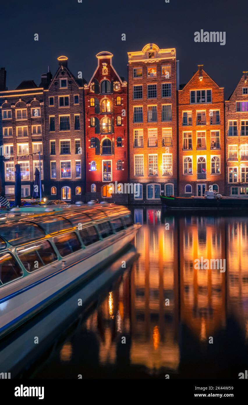 Netherlands. Night Amsterdam. Tourist boat and colorful windows of authentic houses by the water Stock Photo