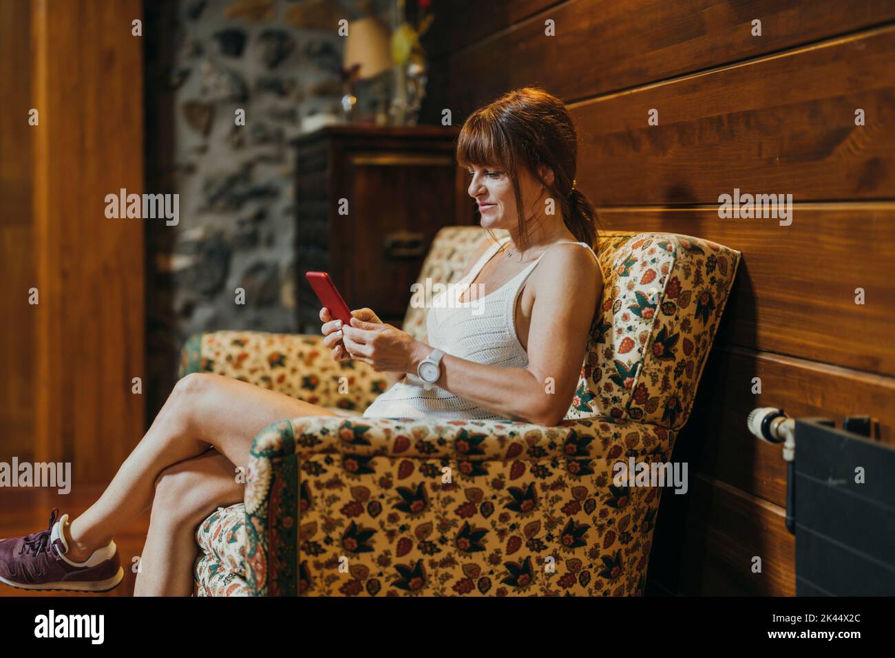 woman sitting on a sofa inside a hotel reading her cell phone Stock Photo