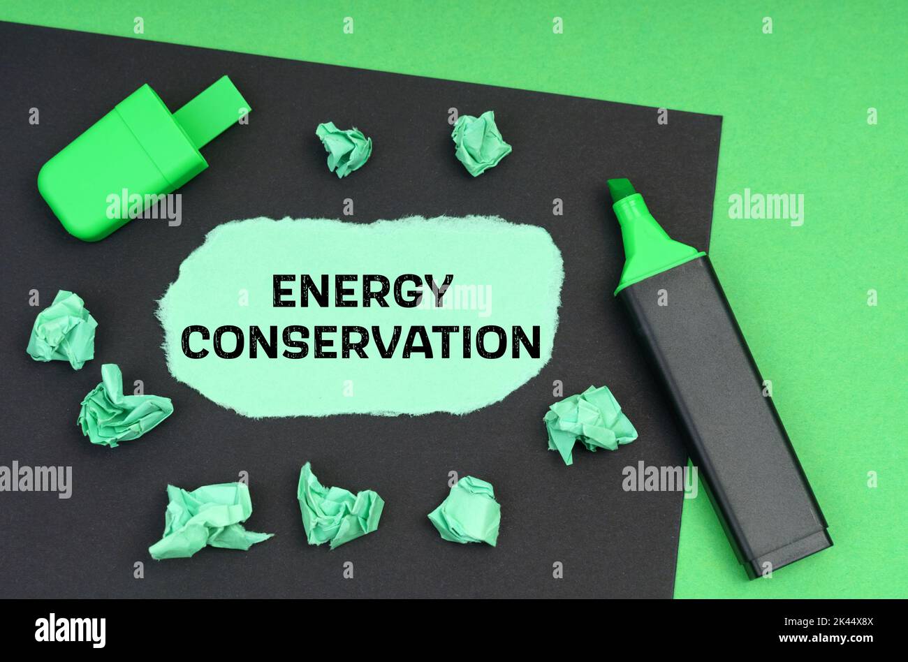 Ecology concept. On a green background, a marker, a black sheet and torn paper with the inscription - Energy Conservation Stock Photo