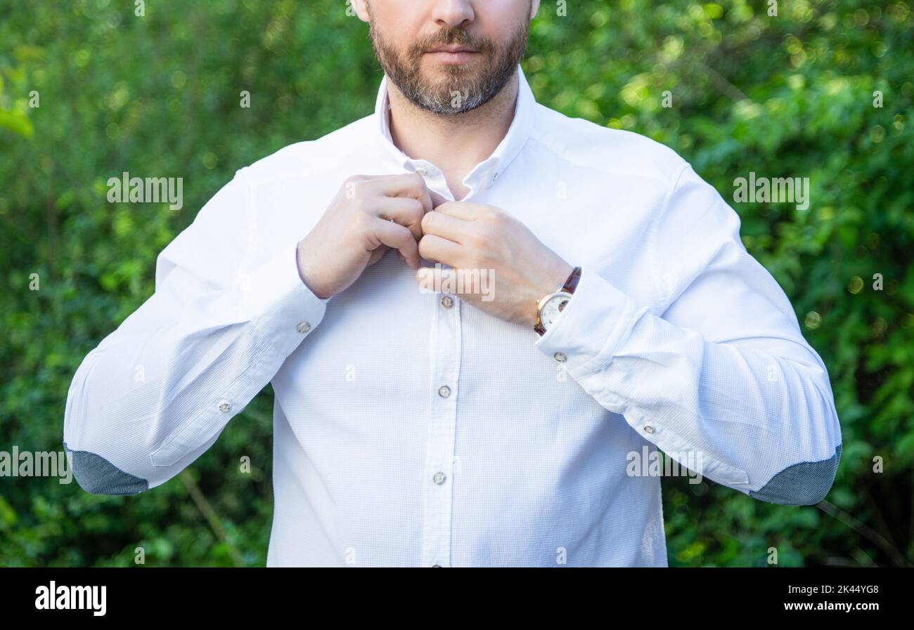 Professional unshaven guy crop view buttoning shirt natural background Stock Photo