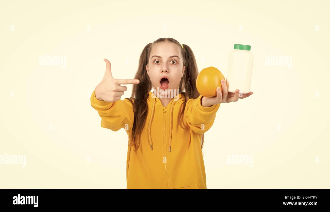 kid pointing finger on orange fruit and vitamin pill in jar bottle isolated on white, surprise. Stock Photo