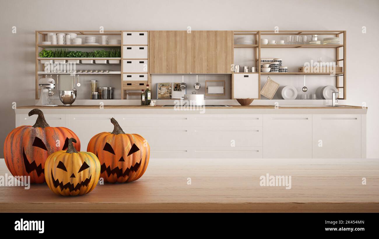 Halloween carved pumpkins on wooden table. Autumn decoration over interior design scene. White modern kitchen with wooden details Stock Photo