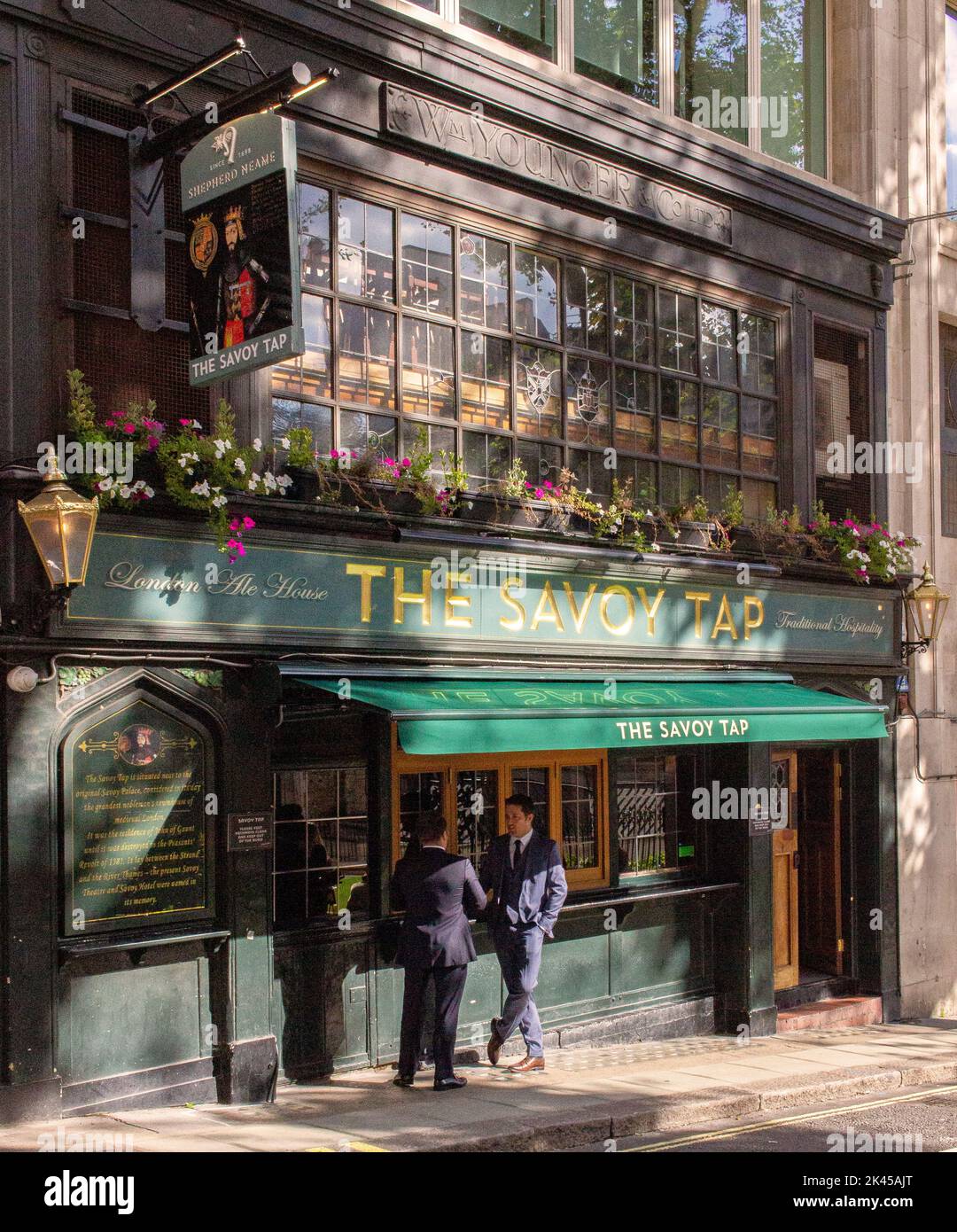 Two young men standing in dappled light and shadows outside The Savoy Tap pub (public house), 2 Savoy St, London Stock Photo