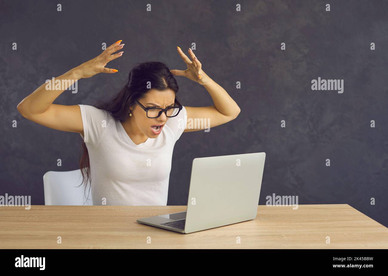 Angry and frustrated woman feels stressed and screams furiously while sitting in front of a laptop. Stock Photo