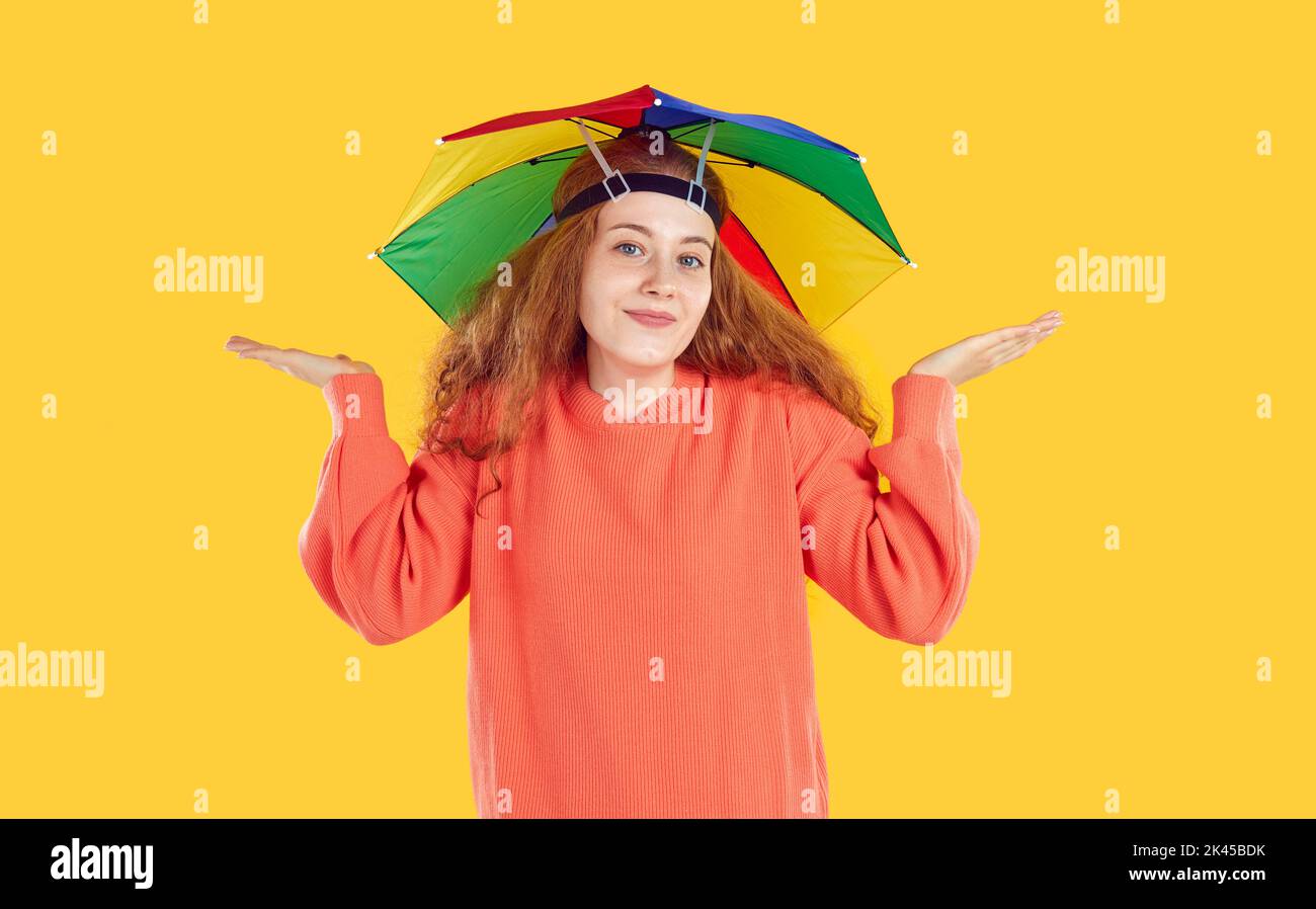 Portrait of happy clueless young woman in funny umbrella hat shrugging her shoulders Stock Photo