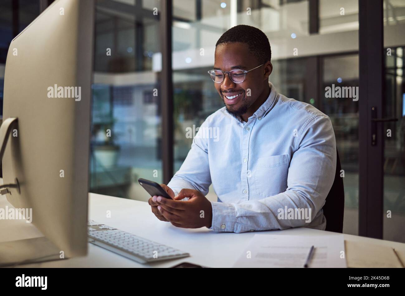 Social media phone, night work and businessman reading an email on smartphone while working in a dark office at night. Corporate African manager in Stock Photo