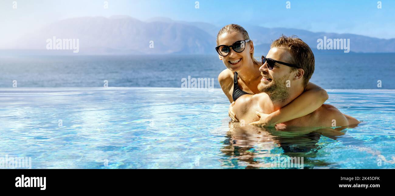 happy couple in love having fun together in infinity swimming pool with sea view at adult resort. romantic summer vacation. honeymoon travel. banner w Stock Photo