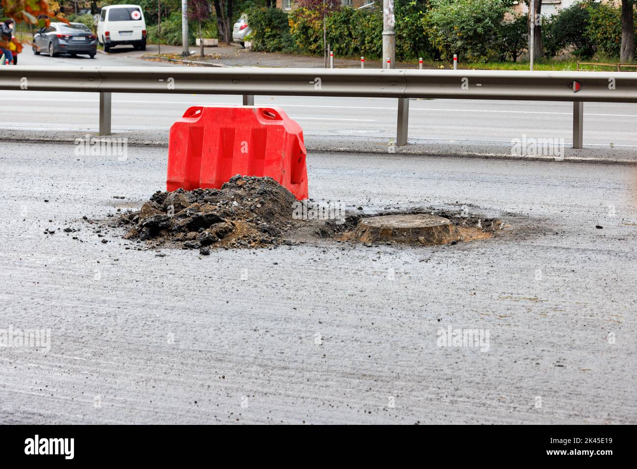A red road barrier warns drivers of road hazards and blocks a manhole being repaired. Copy space. Stock Photo