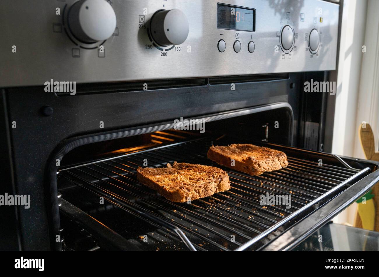 Making toast with brown granary bread under an electric grill in kitchen  Photograph taken by Simon Dack Stock Photo