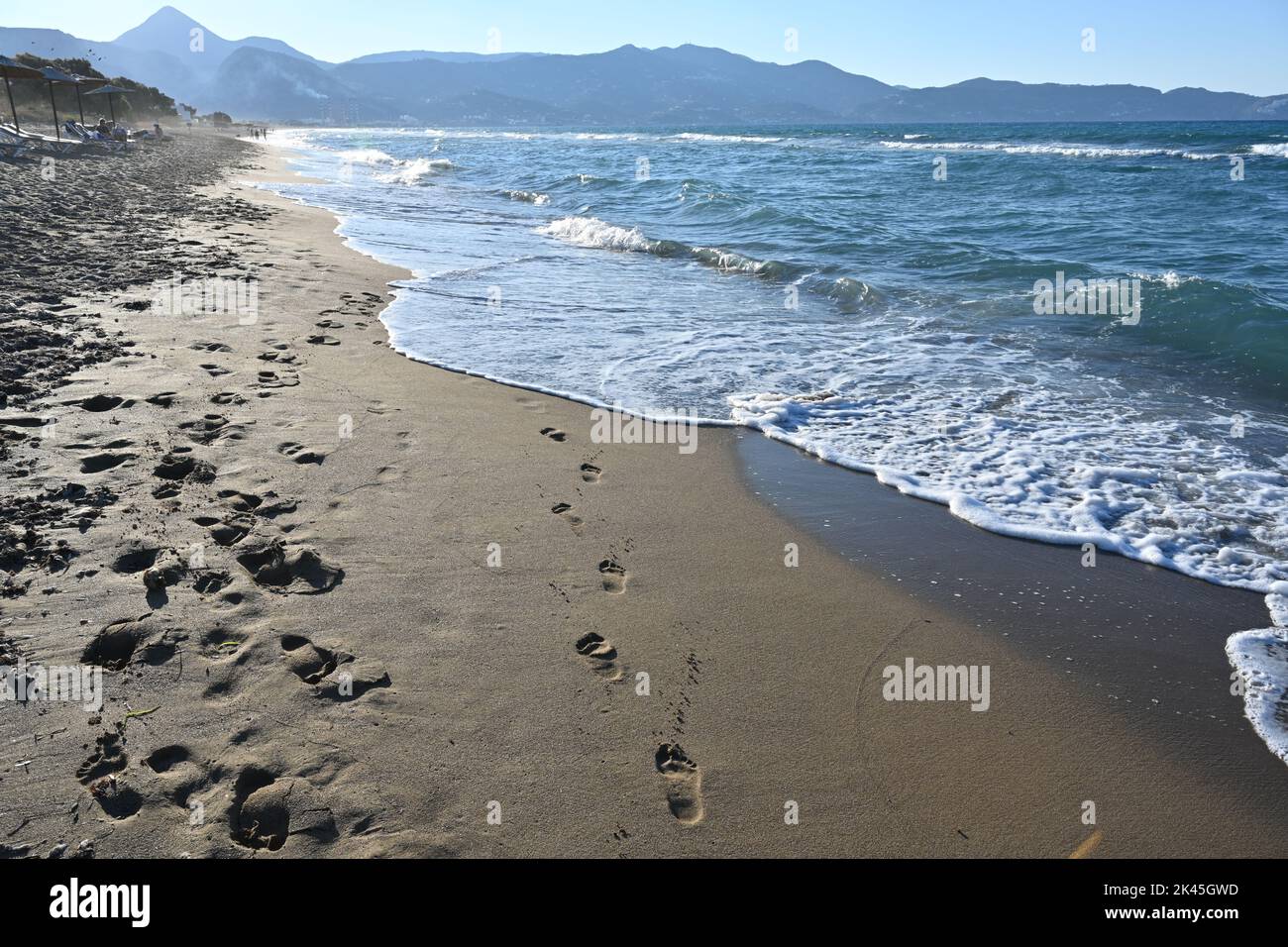 Sandy beach with footprints in the wet sand. Soft waves are washing away the footprints. Stock Photo