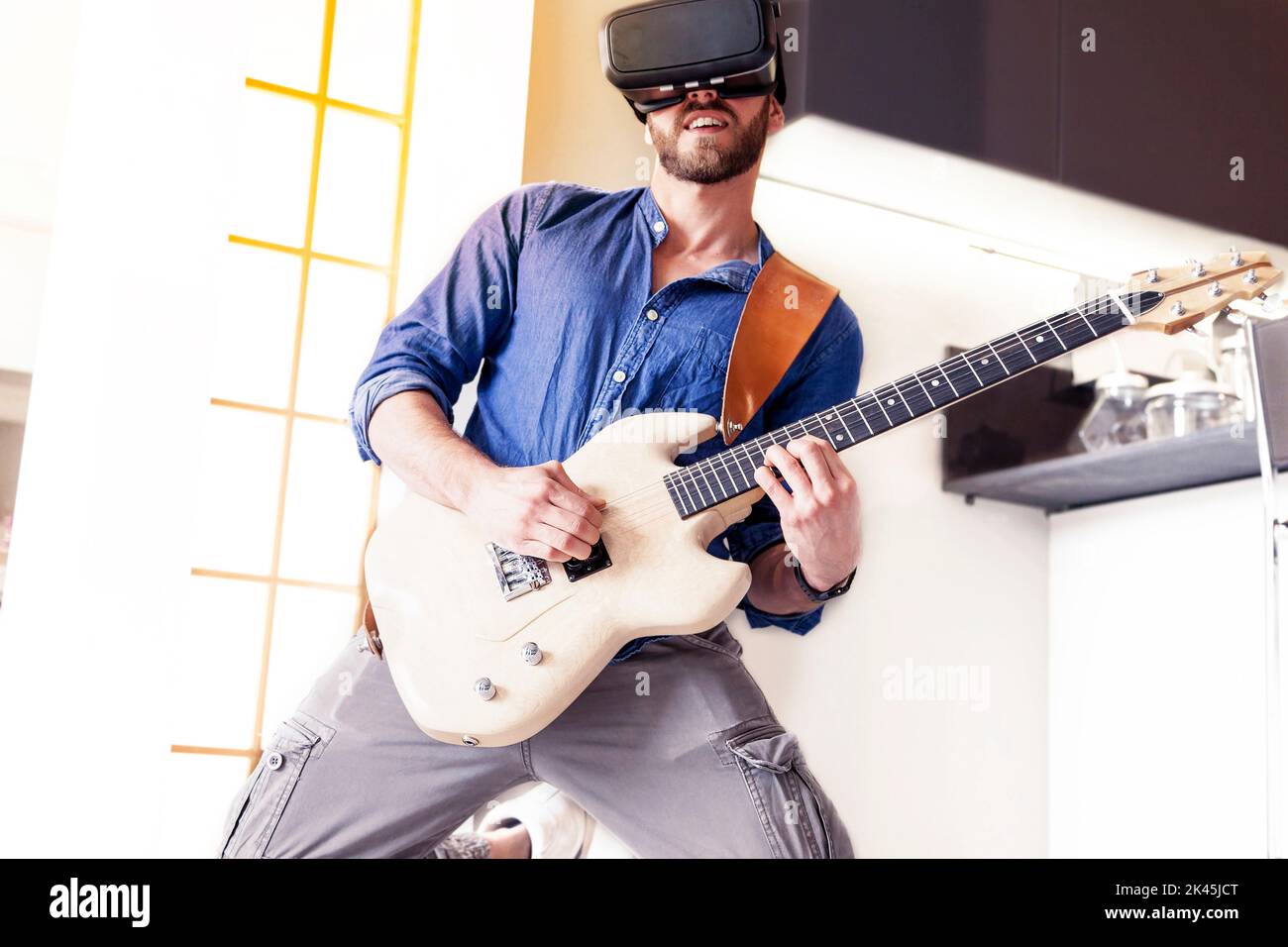 young adult playing guitar at home using viewer for augmented reality Stock Photo