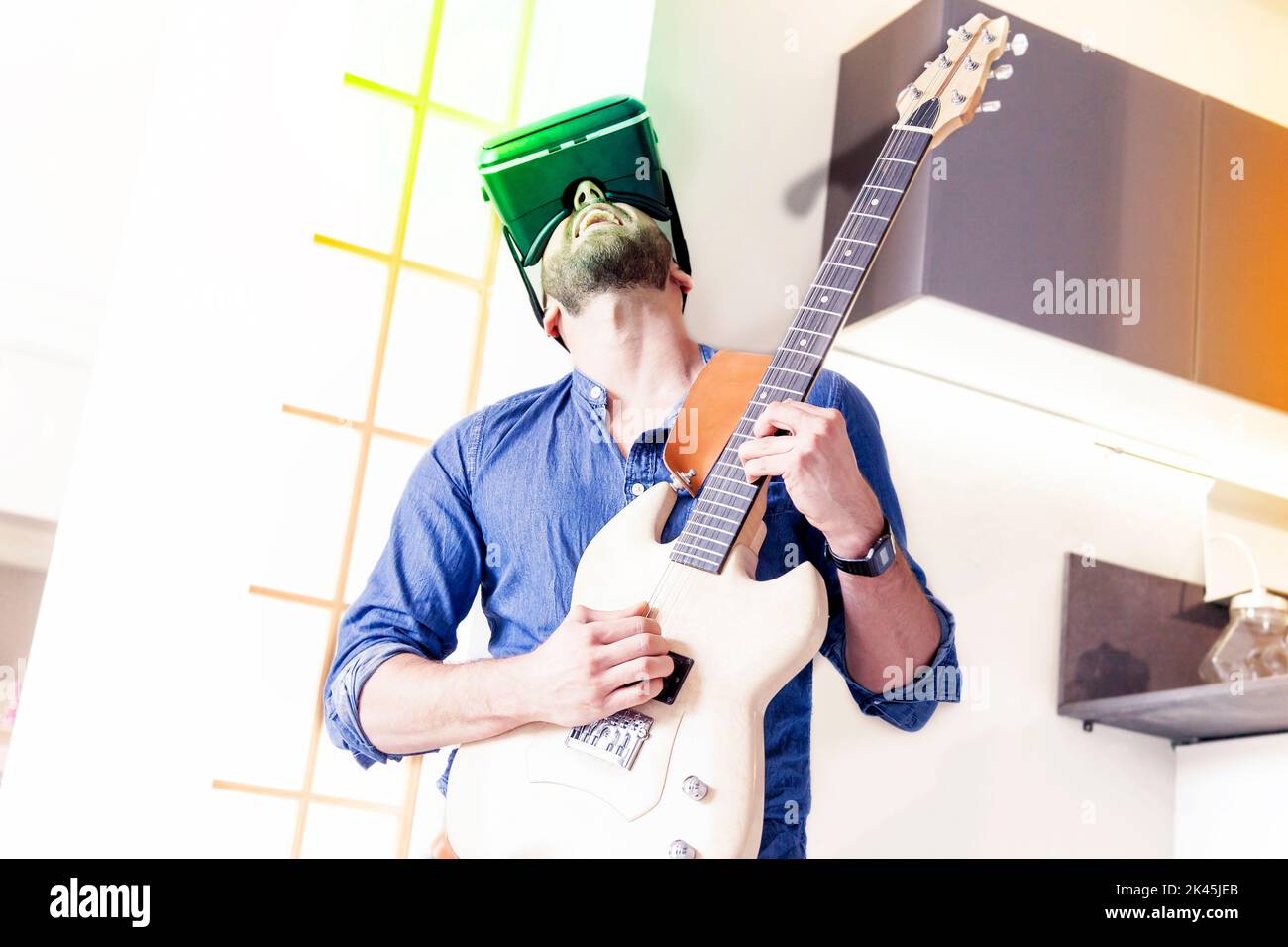 young adult playing guitar at home using viewer for augmented reality Stock Photo