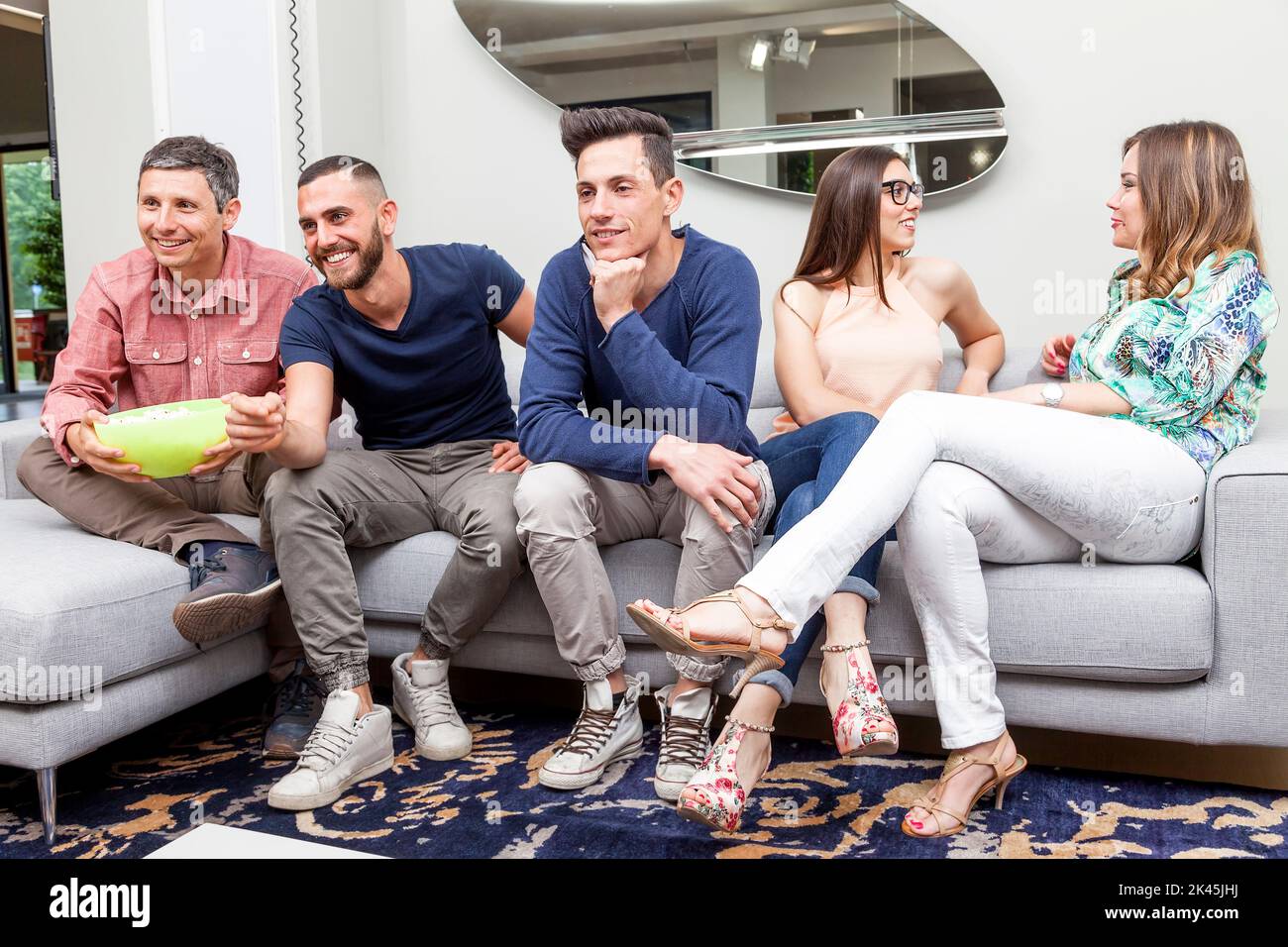group of friends watching tv and eating popcorn on sofa Stock Photo