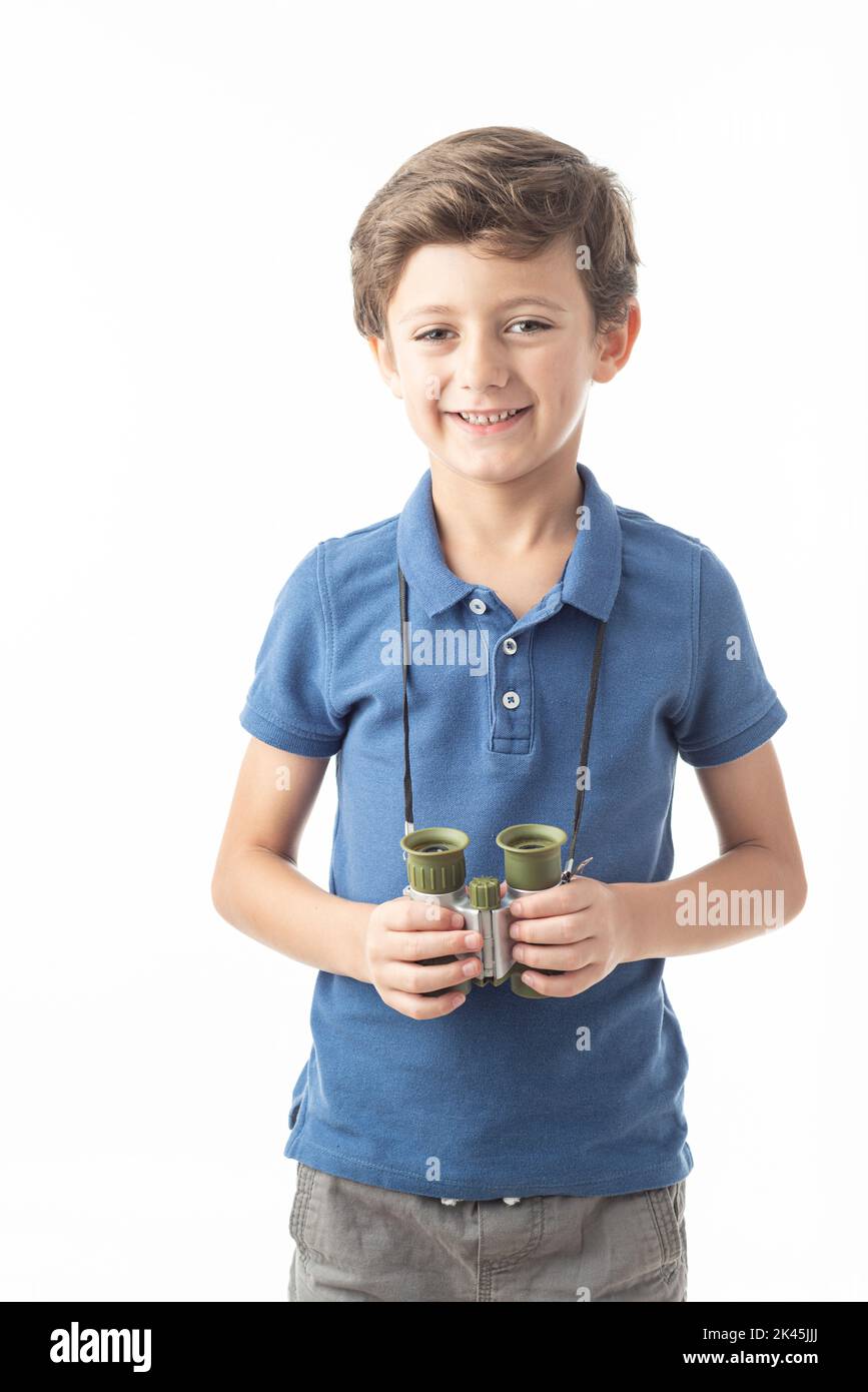 Caucasian child in blue T-shirt looking at camera with binoculars hanging around his neck and smiling expression, on white background. Stock Photo