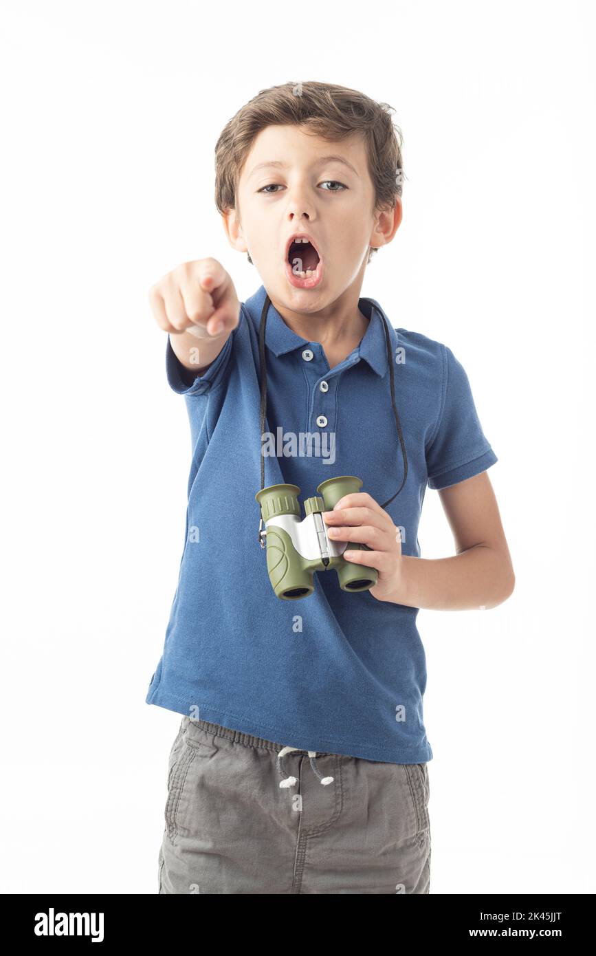 Caucasian child in blue T-shirt looking at camera with binoculars hanging around his neck, with surprised expression and pointing finger, on white bac Stock Photo