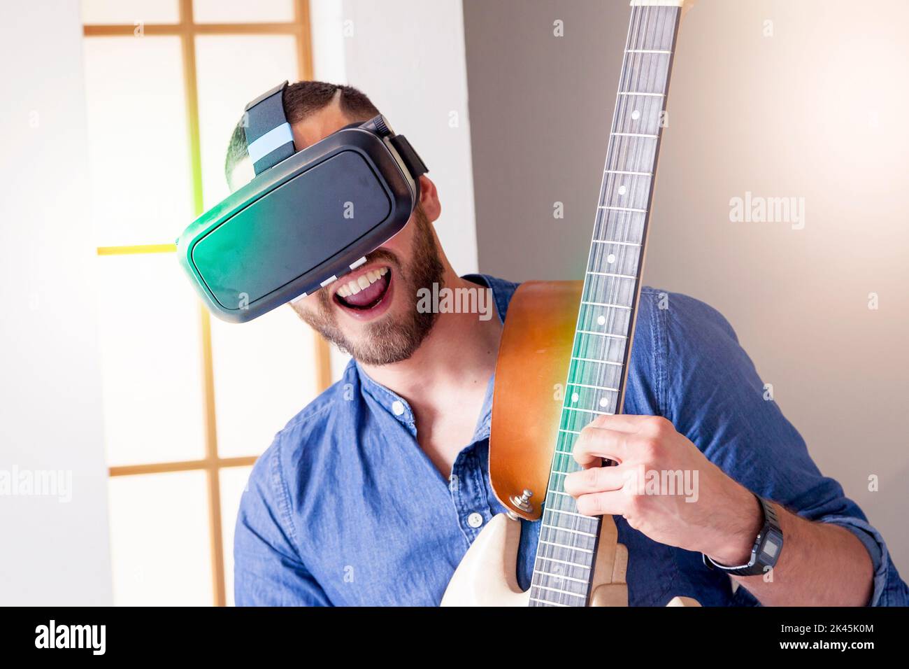 young adult playing guitar at home using viewer for virtual reality Stock Photo