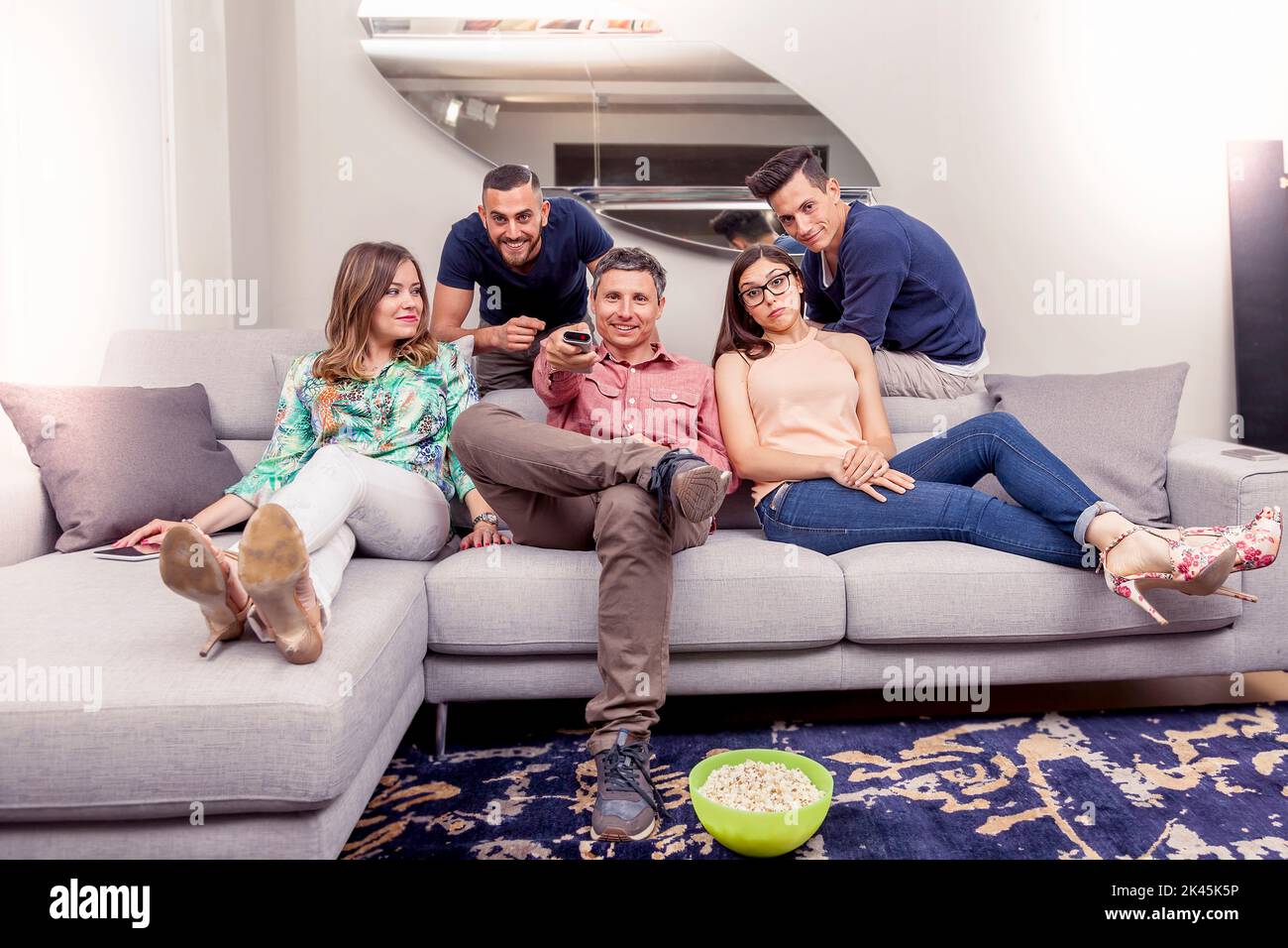 group of friends sitting on the couch turns on the TV with the remote control Stock Photo