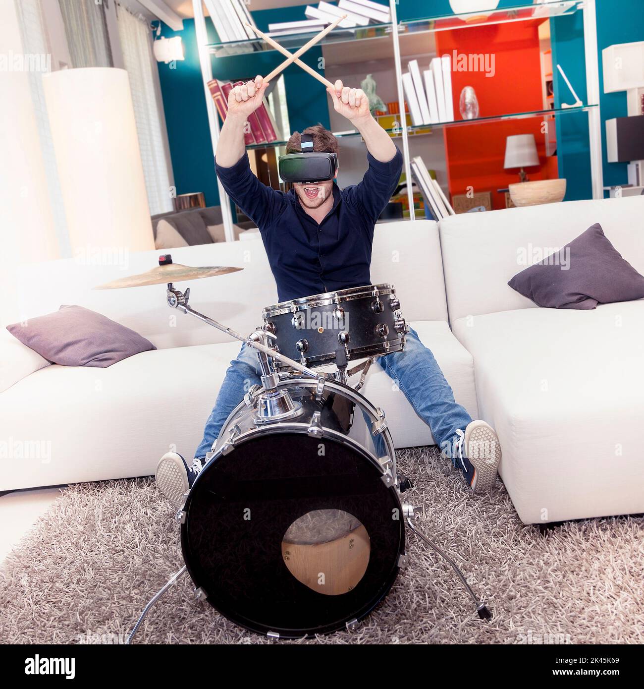 young adult playing drums at home using viewer for virtual reality Stock Photo
