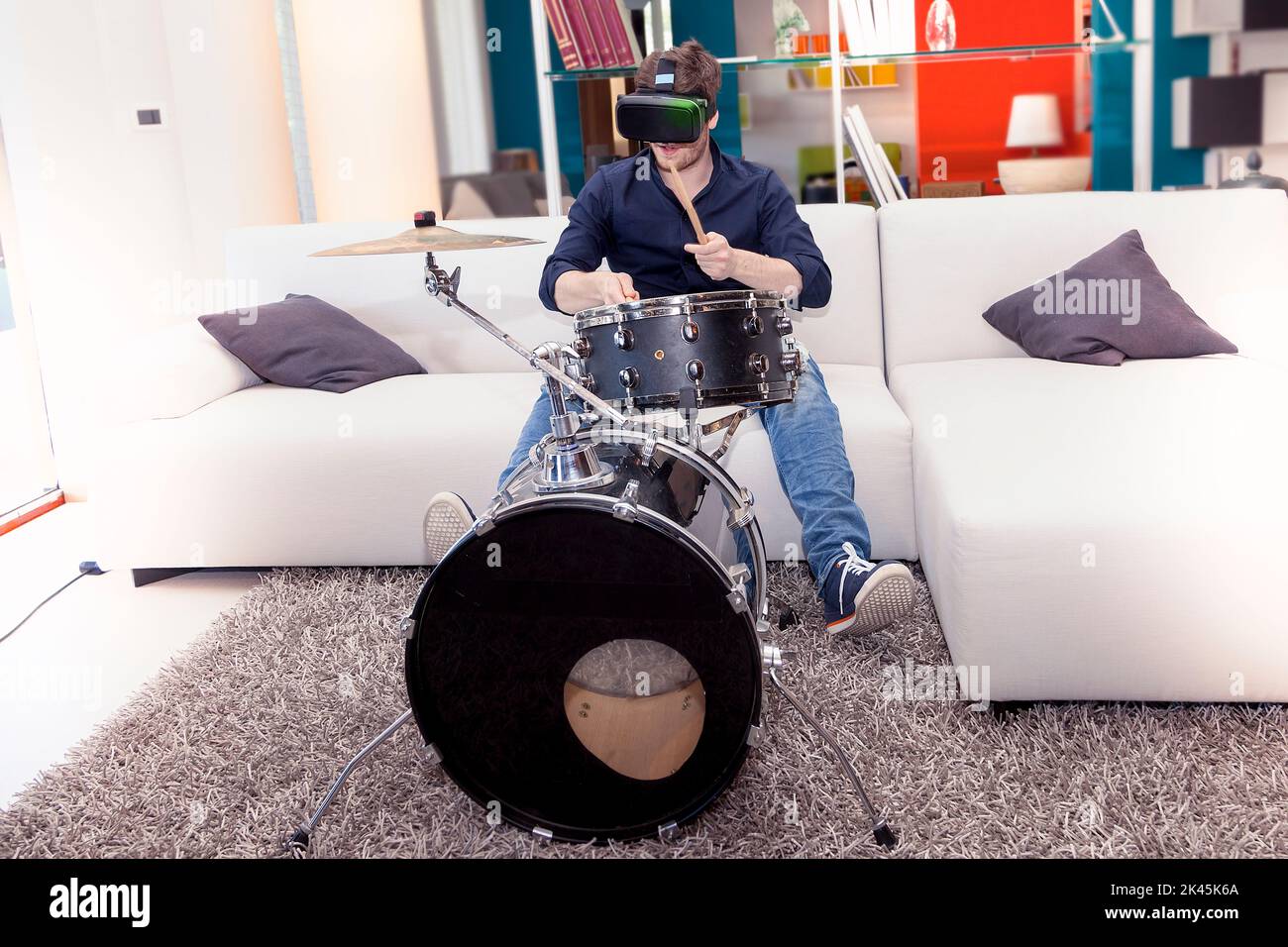 young adult playing drums at home using viewer for virtual reality Stock Photo