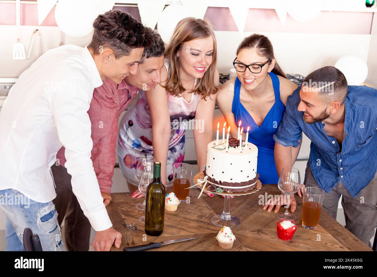 beautiful girl is blowing the candles of her birthday cake with his friends Stock Photo